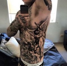 a man with tattoos on his back holding a cell phone in his hand and taking a selfie