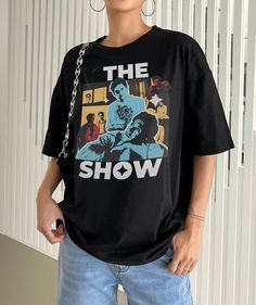 a woman standing in front of a white wall wearing a black t - shirt with the show on it