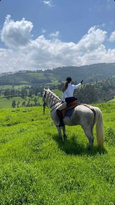 a woman riding on the back of a white horse in a lush green field under a blue sky