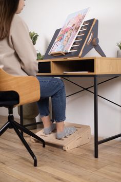 a woman sitting at a desk with an easel on top of it and her feet propped up