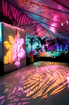 the inside of a tent is lit up with colorful lights and palm trees in the background