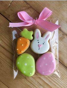 decorated cookies in the shape of bunnies and carrots on a wooden table with pink ribbon