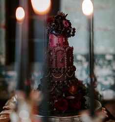 a three tiered chocolate cake with red flowers on top and candles in the background