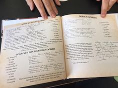 two hands are holding an open book with some writing on it and coffee cup in the background