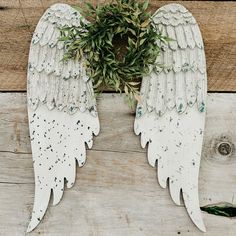 two white angel wings with green leaves on the side of a wooden planked wall