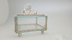 a clear glass shelf with an ornate handle and bead trimmings on the bottom