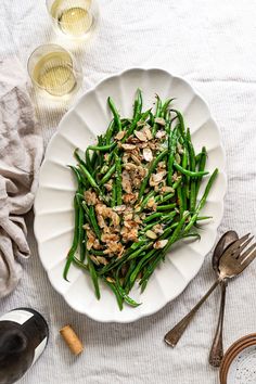 a white plate topped with green beans next to two glasses of wine and utensils