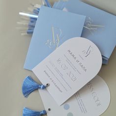 the wedding stationery is laid out on top of each other with blue tassels