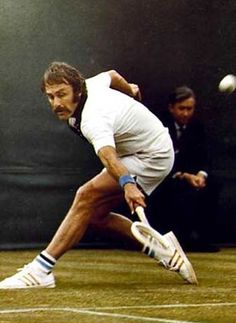 a man swinging a tennis racquet at a ball on a court with two men in the background