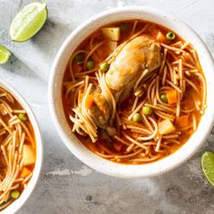 two bowls filled with chicken noodle soup and garnished with limes on the side