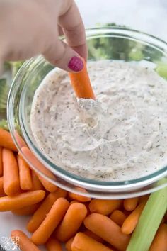 a person dipping dip into a bowl of carrots and celery