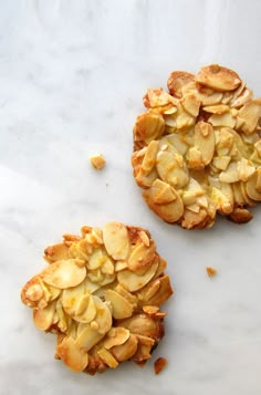 two pastries with almonds on them sitting on a white counter top next to each other