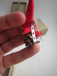 a hand holding a pair of scissors with a pine cone attached to the end of it