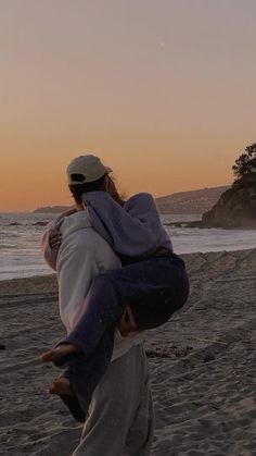 a man carrying a woman on his back while walking along the beach at sunset or dawn