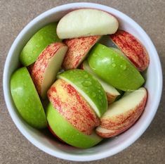 a white bowl filled with green and red apples on top of a brown countertop