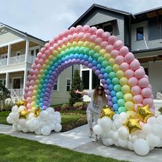 a woman standing in front of a rainbow shaped arch with balloons on the ground and stars