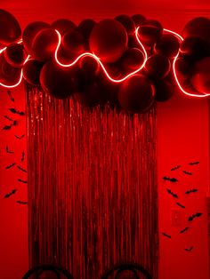 balloons and streamers hanging from the ceiling in a room with red lighting, bats on the wall