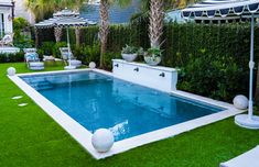 an empty swimming pool surrounded by lawn chairs and umbrellas with palm trees in the background