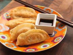 an orange plate topped with dumplings and dipping sauce next to chopsticks on a wooden table