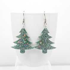 Fun Christmas tree dangle earrings featuring Frosty Green glitter with Rainbow shards mixed with crystal clear epoxy resin, and finished with Stainless Steel ear wires with soft silicone backs.  Clear epoxy coated for a glossy protective layer.  Festive holiday earrings measure 2 1/2 inches long and 1 1/2 inches wide and are very lightweight.  These earrings make the perfect Christmas party accessory, stocking stuffer and Secret Santa gift.   ⭐ CARE   Wipe clean with a soft cloth (such as an eyeglass cleaning cloth).  Do not use alcohol or acetone as this will damage the glossy surface.  It is not recommended to wear in water.  Do not expose to extreme heat.  To extend the life of your resin pieces, store separately from other jewelry and keep out of direct sunlight whenever possible. Christmas Party Jewelry With Sparkling Details, Sparkling Christmas Party Jewelry, Sparkling Jewelry For Christmas Party, Green Jewelry For New Year's Party, Green Jewelry For New Year Party, Christmas Party Accessories, Crystal Clear Epoxy Resin, Jewelry Holiday, Clear Epoxy Resin