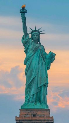 the statue of liberty in new york city, ny at sunset with clouds behind it