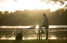 a man sitting at a picnic table next to a lake with a fishing rod on it