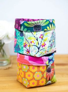 three colorful boxes sitting on top of a wooden table next to a vase with flowers