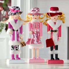 three toy figurines dressed in pink, white and red outfits are standing next to each other