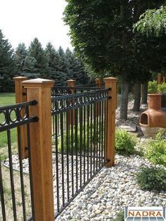 an iron and wood fence in the middle of a yard with rocks, grass and trees