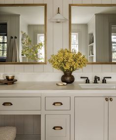 a bathroom sink with two mirrors above it and a vase filled with flowers on the counter