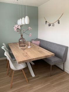 a dining room table and bench with flowers in vase on the top, along with hanging lights