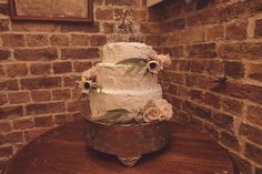 a wedding cake sitting on top of a table in front of a brick wall with flowers