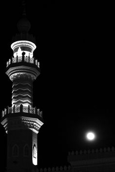 a tall tower lit up at night with the moon in the sky behind it,