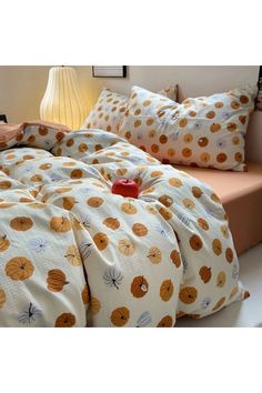 a bed covered in lots of pillows and blankets with orange pumpkins on the covers