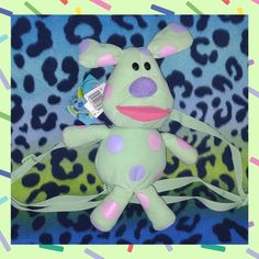 a green stuffed animal with polka dots on it's face and neck, sitting in front of a leopard print background