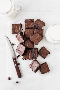 chocolate brownies cut into squares on a cutting board next to a cup of milk