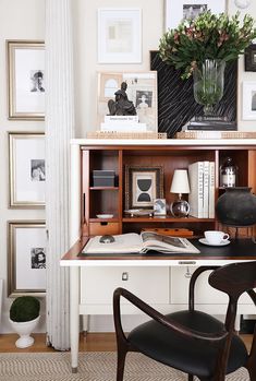 a desk with some pictures on the wall and a chair next to it in front of an open bookcase