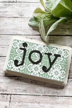 a green and white tile coaster with the word joy on it next to a plant