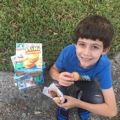 a young boy sitting on the ground holding a doughnut and some cereals next to him