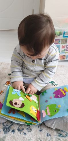 a baby is sitting on the floor reading a book with animals and fish decorations around it