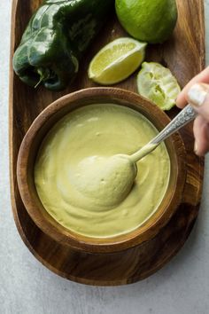 a wooden bowl filled with guacamole surrounded by limes and jalapenos