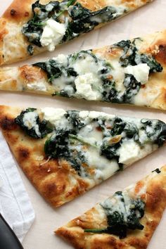 four slices of pizza with spinach and cheese on them sitting on a white surface