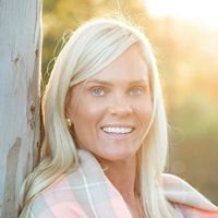 a woman standing next to a tree smiling at the camera with sunlight shining on her face