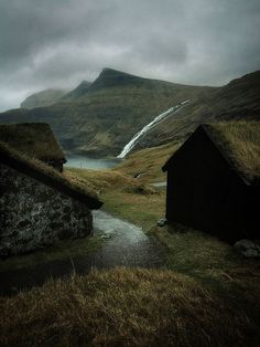 two small houses with grass roofs on the side of a mountain in iceland, one has a waterfall coming out of it