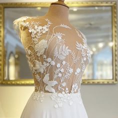 the back of a white wedding dress on display in front of a mirror and gold framed mirror