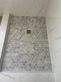 a bathroom shower with hexagon tile on the floor, and a drain in the middle