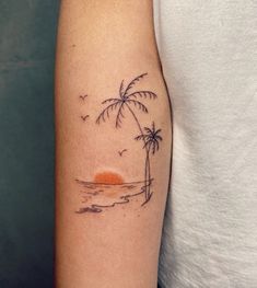 a woman's arm with a small palm tree on the beach and an orange sun