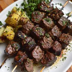 a white plate topped with meat and veggies on skewers next to broccoli