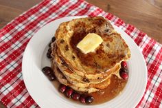 a stack of pancakes with butter and berries on a plate next to a red checkered napkin