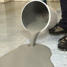 a man is pouring cement into a bucket on the floor with his foot in it